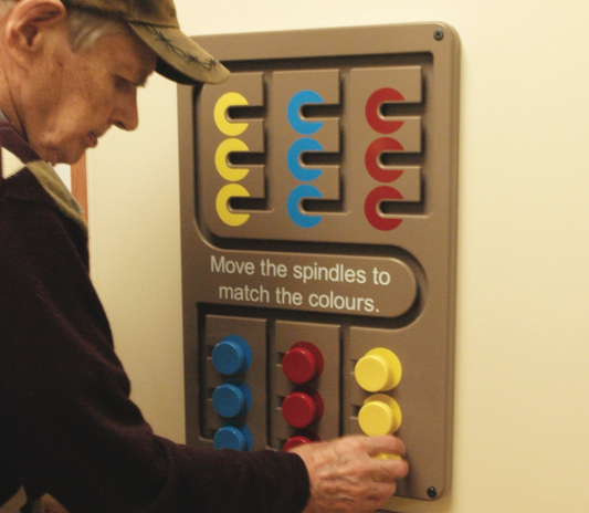 three spindles in three different colours are at the bottom of a wooden board. There are tracks to move the spindle into coloured targets on the top of the board. Text is written in the middle saying "move the spindles to match the colours"
